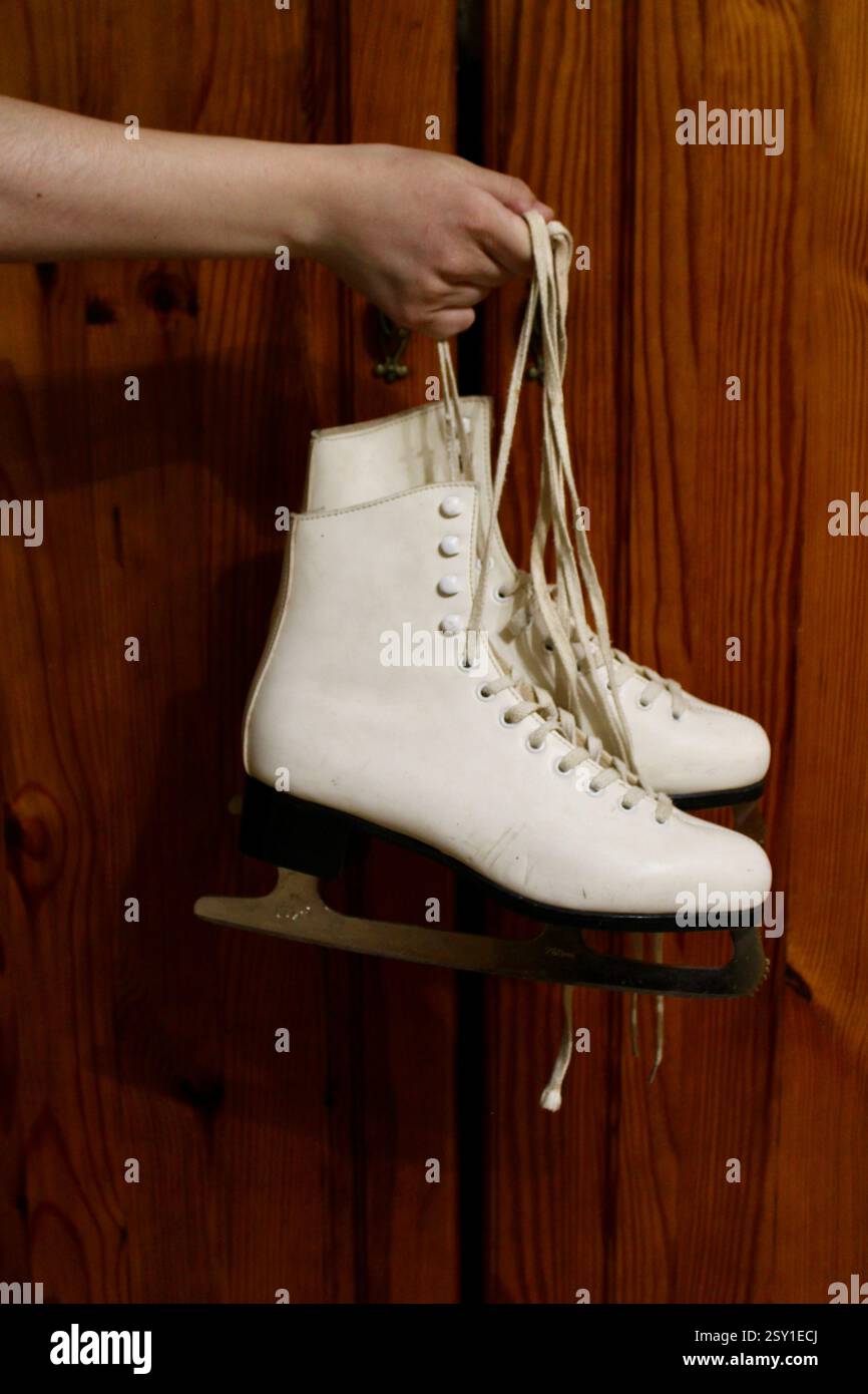 Giovane donna che tiene un paio di pattini di pelle bianca, si prepara per gli sport invernali, scarpe sportive da donna, femminile, attrezzatura, stile di vita attivo felice. Foto Stock