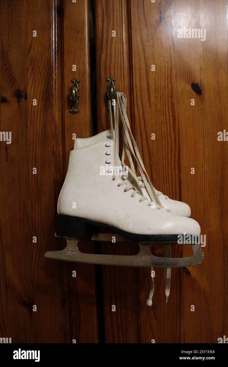 Un paio di pattini di ghiaccio in pelle bianca appesi al gancio dell'armadio in legno della camera da letto, per prepararsi agli sport invernali, scarpe sportive da donna, femminili Foto Stock