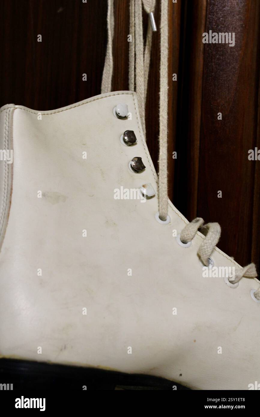 Un paio di pattini di ghiaccio in pelle bianca appesi al gancio dell'armadio in legno della camera da letto, per prepararsi agli sport invernali, scarpe sportive da donna, femminili Foto Stock