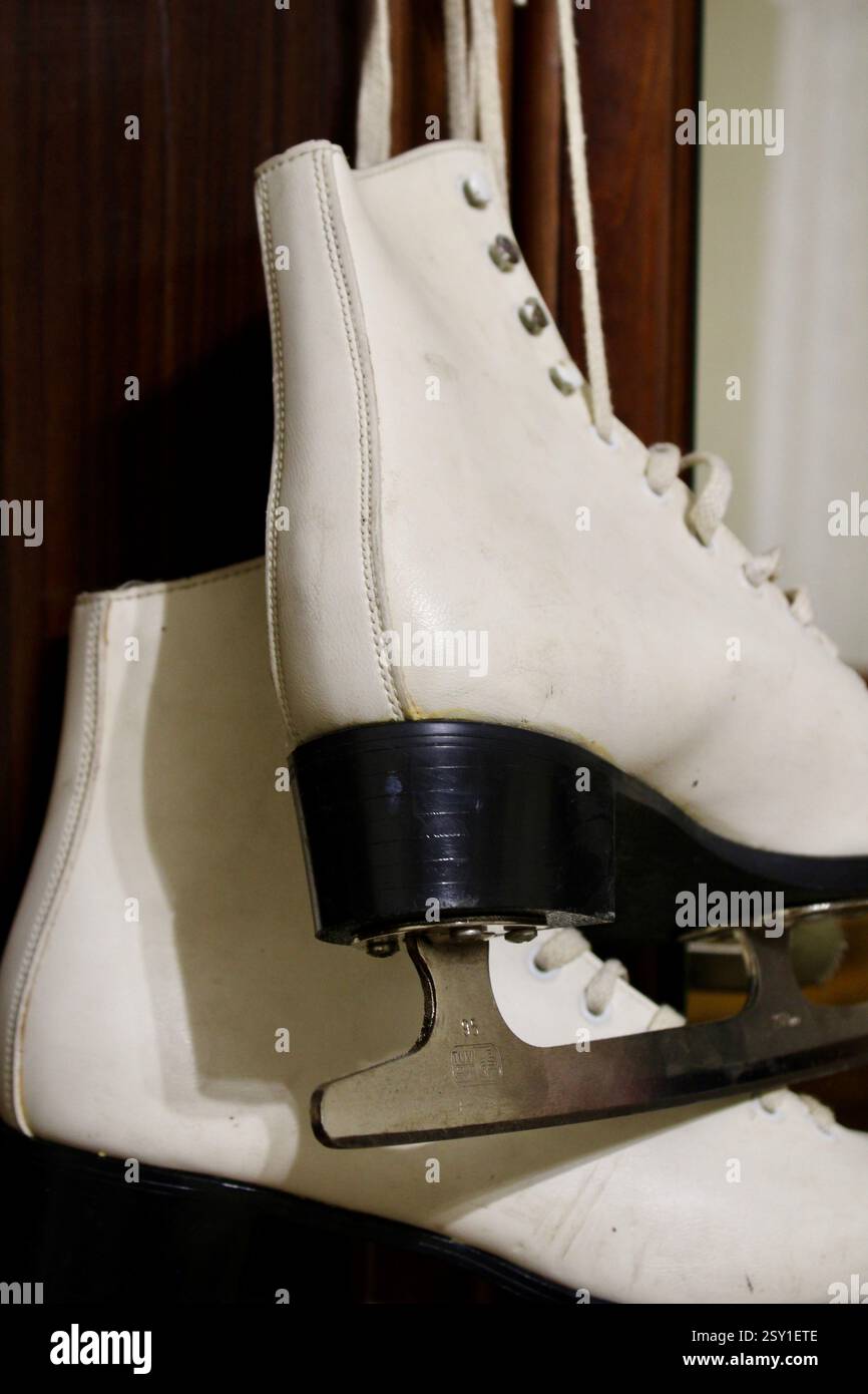 Un paio di pattini di ghiaccio in pelle bianca appesi al gancio dell'armadio in legno della camera da letto, per prepararsi agli sport invernali, scarpe sportive da donna, femminili Foto Stock