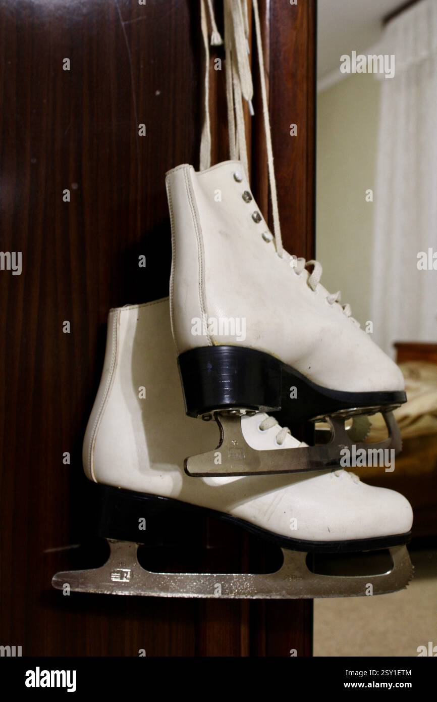 Un paio di pattini di ghiaccio in pelle bianca appesi al gancio dell'armadio in legno della camera da letto, per prepararsi agli sport invernali, scarpe sportive da donna, femminili Foto Stock