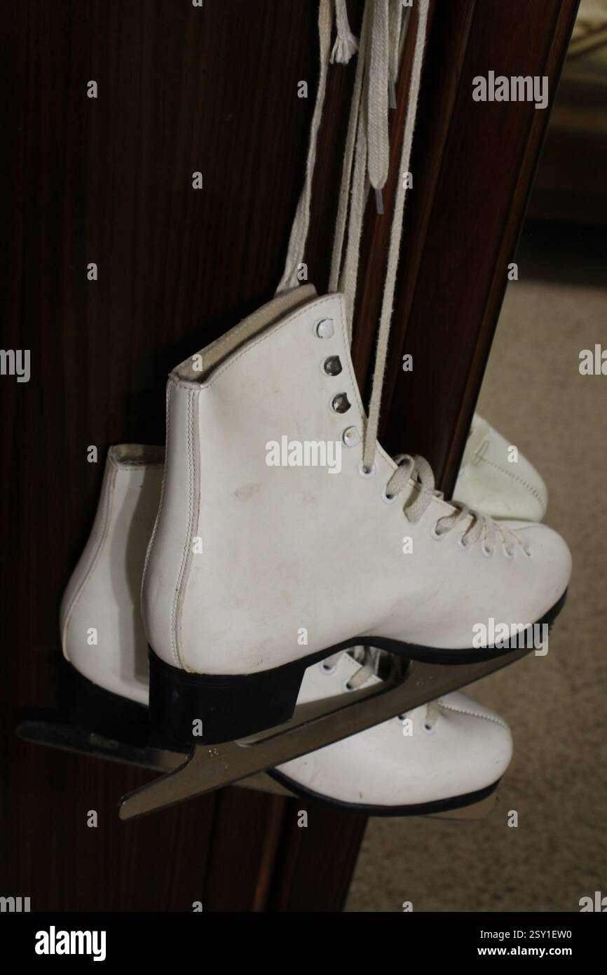 Un paio di pattini di ghiaccio in pelle bianca appesi al gancio dell'armadio in legno della camera da letto, per prepararsi agli sport invernali, scarpe sportive da donna, femminili Foto Stock