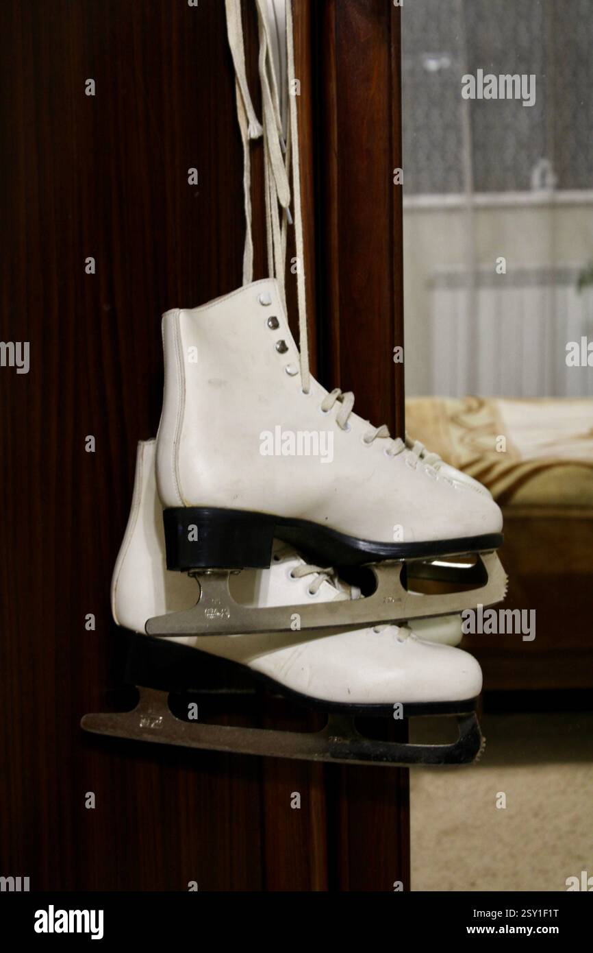 Un paio di pattini di ghiaccio in pelle bianca appesi al gancio dell'armadio in legno della camera da letto, per prepararsi agli sport invernali, scarpe sportive da donna, femminili Foto Stock