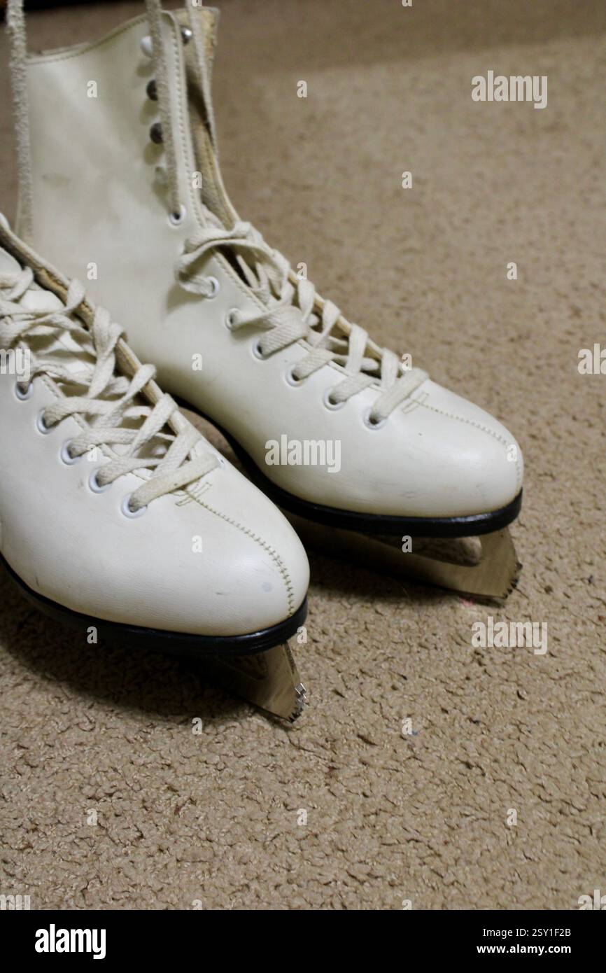 Un paio di pattini da ghiaccio in pelle bianca, sdraiati sul morbido tappeto della camera, pronti per gli sport invernali, scarpe sportive da donna, stile di vita femminile e attivo. Foto Stock