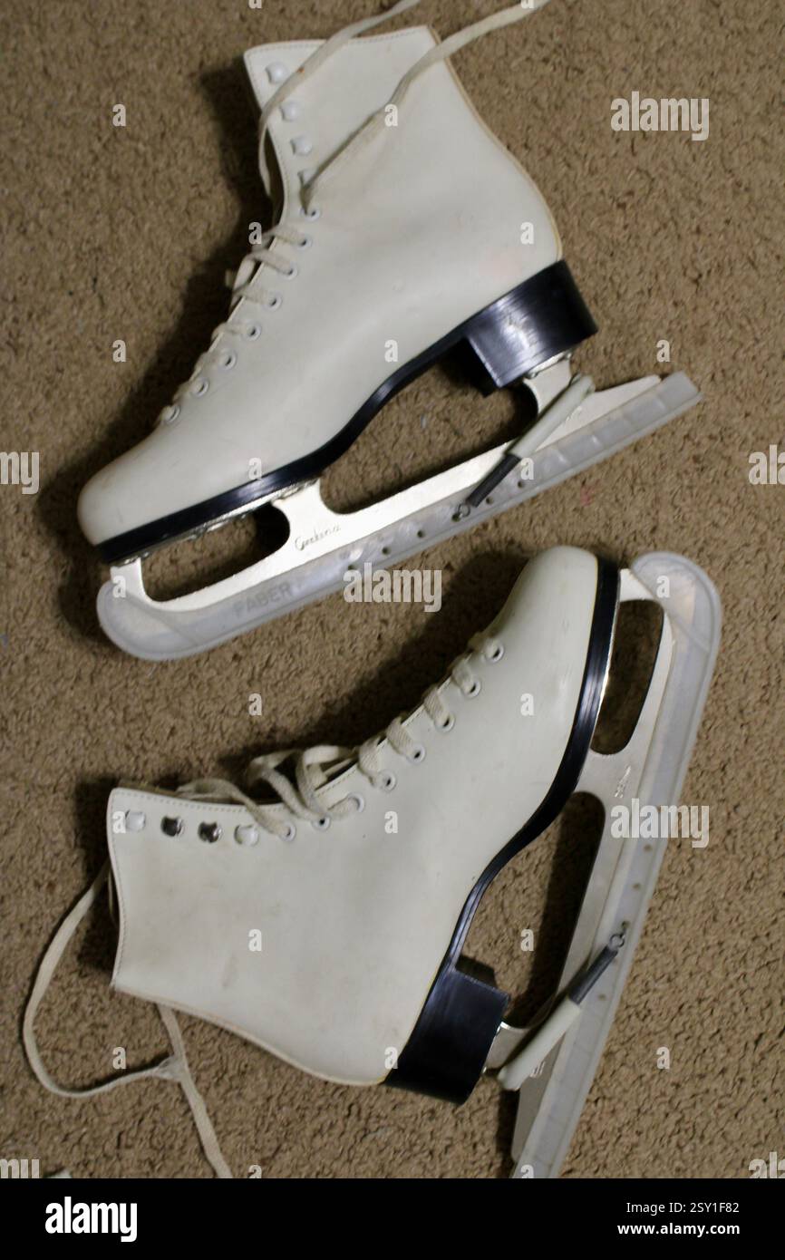 Un paio di pattini da ghiaccio in pelle bianca, sdraiati sul morbido tappeto della camera, pronti per gli sport invernali, scarpe sportive da donna, stile di vita femminile e attivo. Foto Stock