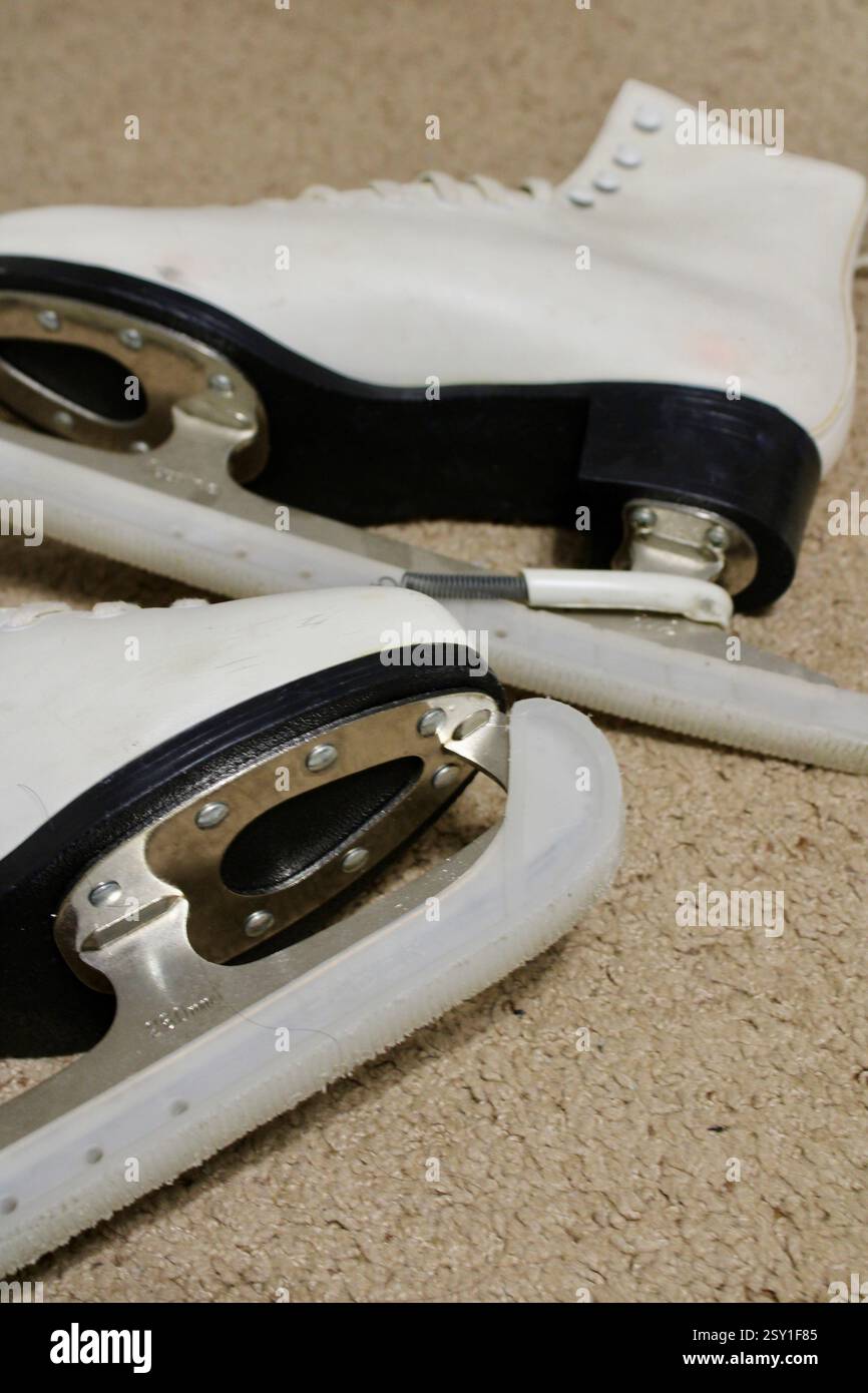 Un paio di pattini da ghiaccio in pelle bianca, sdraiati sul morbido tappeto della camera, pronti per gli sport invernali, scarpe sportive da donna, stile di vita femminile e attivo. Foto Stock