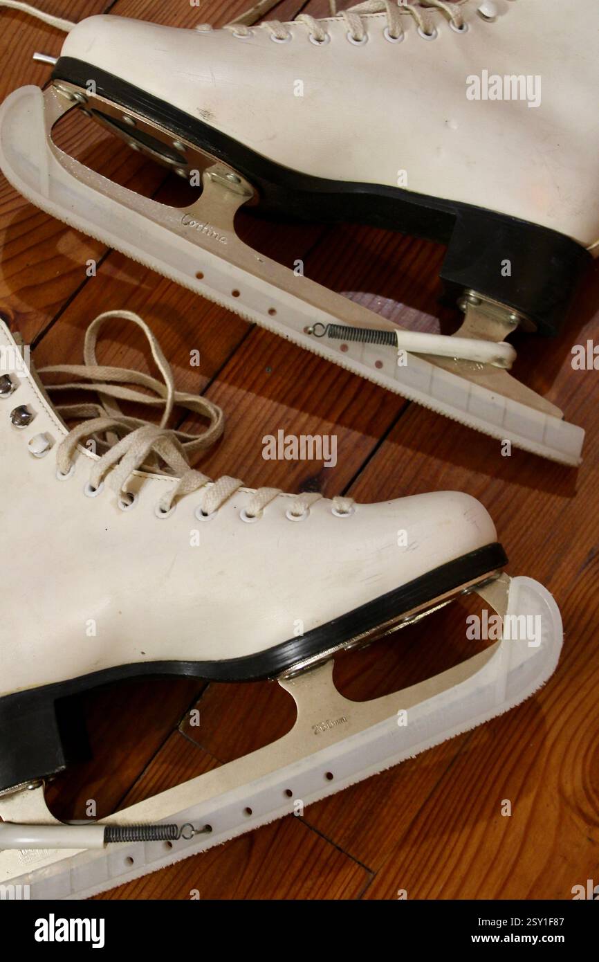un paio di pattini di ghiaccio in pelle bianca che si trovano sul pavimento in legno al coperto, per prepararsi agli sport invernali, alle scarpe sportive da donna, allo stile di vita attivo e alle attrezzature. Foto Stock