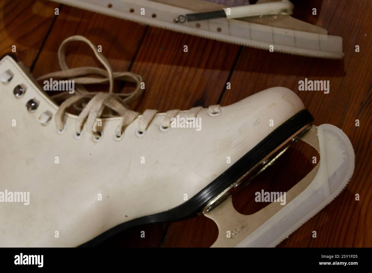 un paio di pattini di ghiaccio in pelle bianca che si trovano sul pavimento in legno al coperto, per prepararsi agli sport invernali, alle scarpe sportive da donna, allo stile di vita attivo e alle attrezzature. Foto Stock