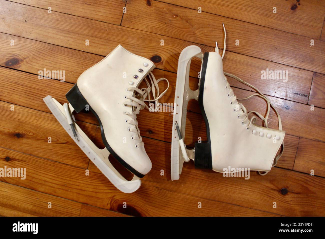 un paio di pattini di ghiaccio in pelle bianca che si trovano sul pavimento in legno al coperto, per prepararsi agli sport invernali, alle scarpe sportive da donna, allo stile di vita attivo e alle attrezzature. Foto Stock
