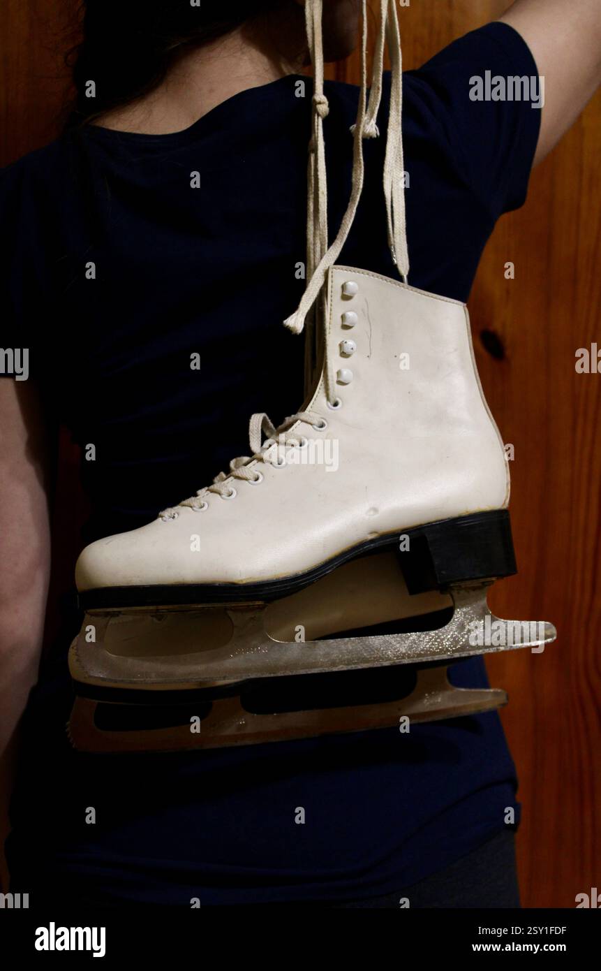 Giovane donna che tiene un paio di pattini di pelle bianca, si prepara per gli sport invernali, scarpe sportive da donna, femminile, attrezzatura, stile di vita attivo felice. Foto Stock