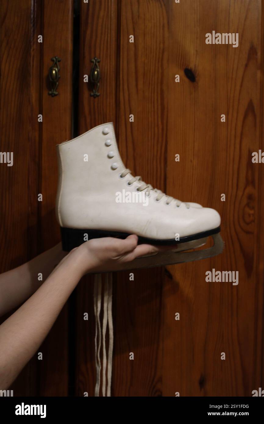 Giovane donna che tiene un paio di pattini di pelle bianca, si prepara per gli sport invernali, scarpe sportive da donna, femminile, attrezzatura, stile di vita attivo felice. Foto Stock