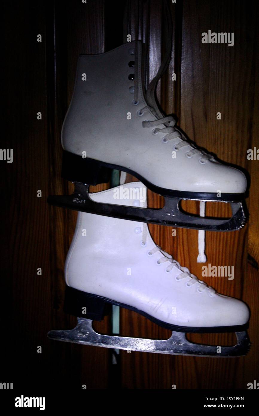 Un paio di pattini di ghiaccio in pelle bianca appesi al gancio dell'armadio in legno della camera da letto, per prepararsi agli sport invernali, scarpe sportive da donna, femminili Foto Stock