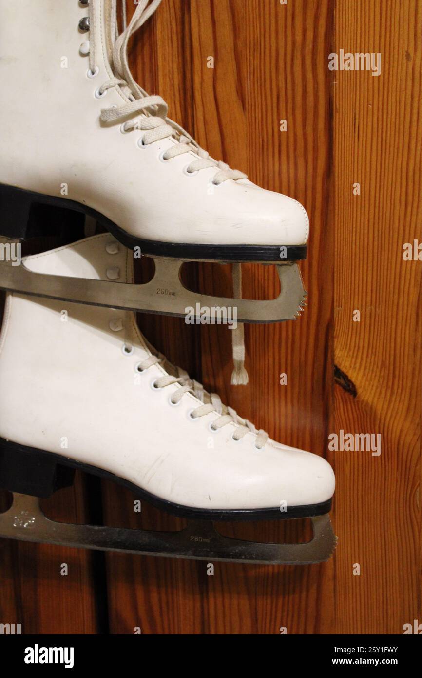 Un paio di pattini di ghiaccio in pelle bianca appesi al gancio dell'armadio in legno della camera da letto, per prepararsi agli sport invernali, scarpe sportive da donna, femminili Foto Stock