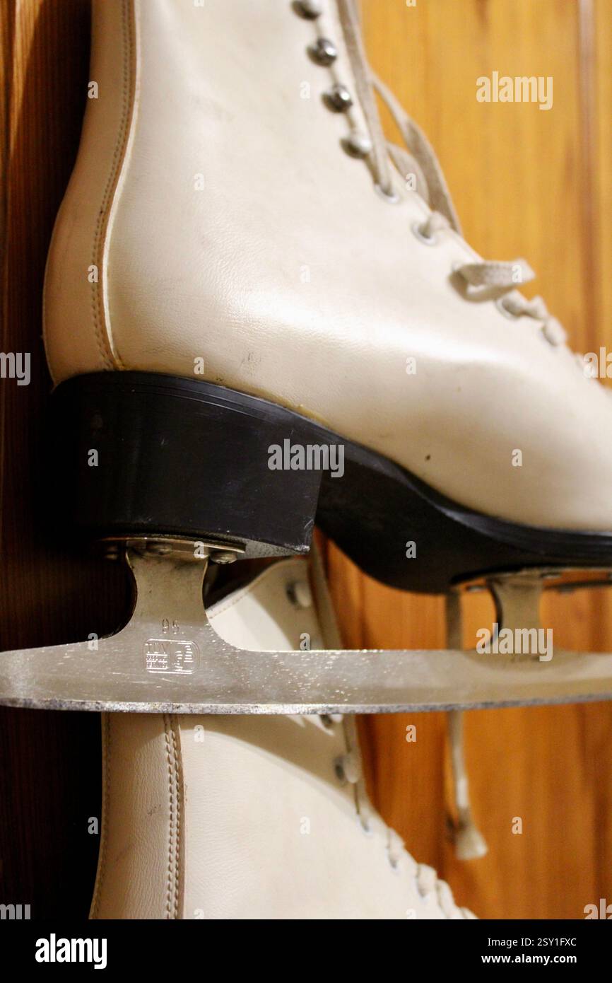 Un paio di pattini di ghiaccio in pelle bianca appesi al gancio dell'armadio in legno della camera da letto, per prepararsi agli sport invernali, scarpe sportive da donna, femminili Foto Stock