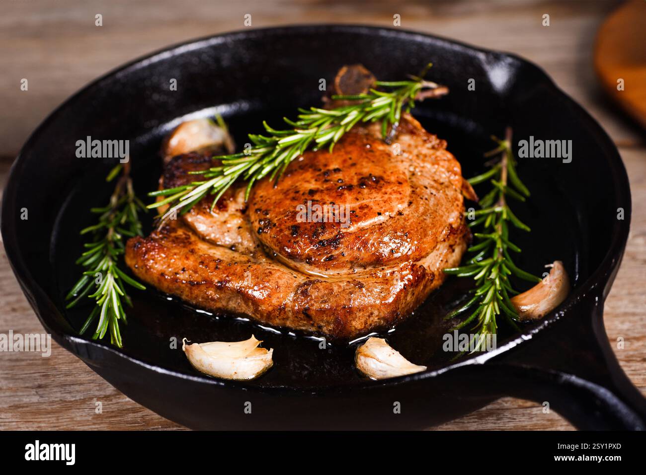 Cotoletta di maiale sull'osso in un pezzo di burro con aglio e rosmarino in una padella Foto Stock