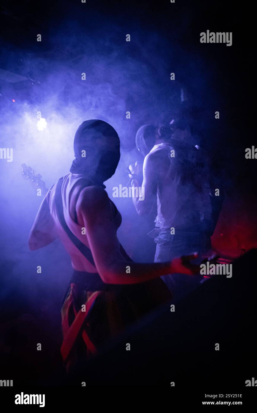 Una spettacolare fotografia di concerti dal vivo con musicisti mascherati immersi in un'intensa illuminazione blu e rossa del palcoscenico. La scena è piena di mistero, energ Foto Stock