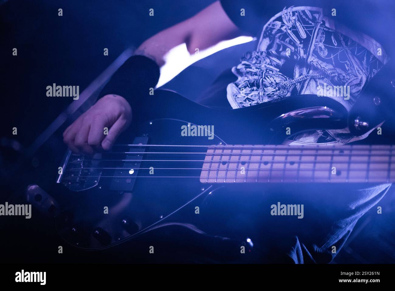 Uno scatto ravvicinato di un bassista che suona sul palco durante un concerto dal vivo. La mano del musicista prende le corde mentre la drammatica luce blu . Foto Stock