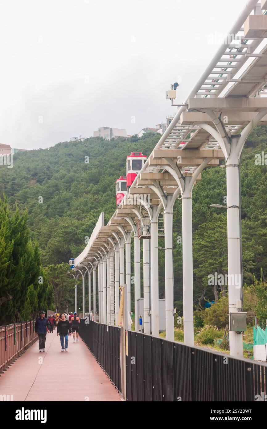 Busan, Corea del Sud - 29 ottobre 2024: Colorati treni a capsula del cielo sulla Busan Green Railway, con un sentiero a piedi e un paesaggio panoramico. Foto Stock