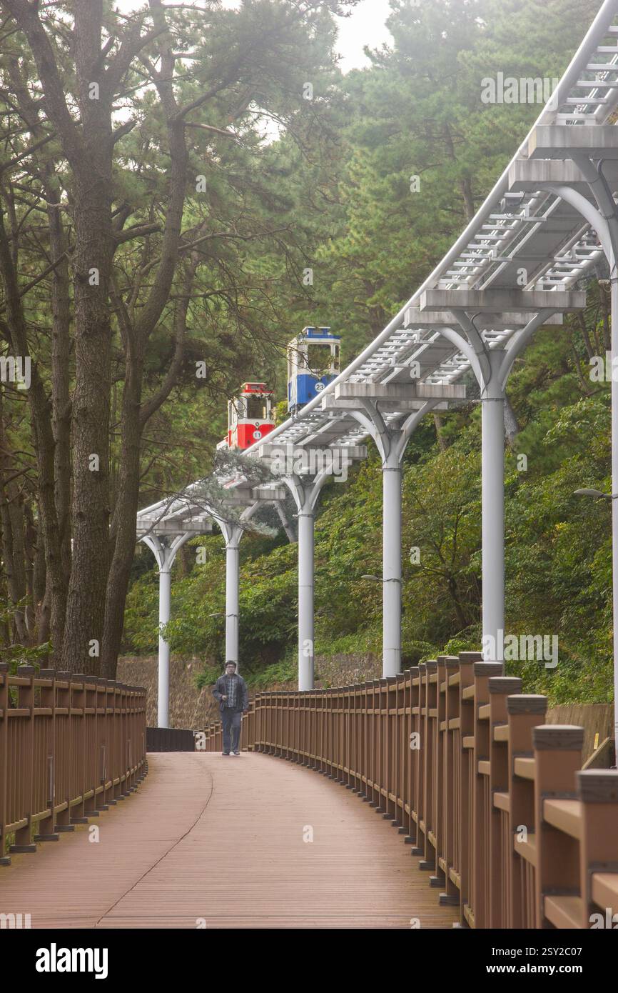 Busan, Corea del Sud - 29 ottobre 2024: Colorati treni a capsula del cielo sulla Busan Green Railway, con un sentiero a piedi e un paesaggio panoramico. Foto Stock
