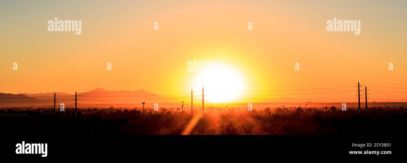Il sole sta tramontando nel cielo sopra un campo. Il sole è molto luminoso e sta gettando un'ombra sul terreno Foto Stock