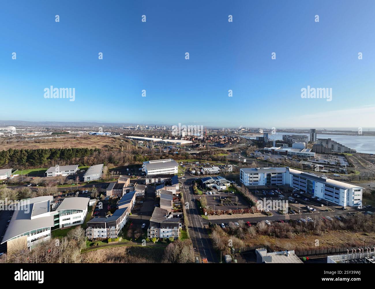Vista aerea di Cardiff che mostra edifici moderni, aree industriali, l'estuario del fiume Severn e spazi verdi, sotto un cielo azzurro Foto Stock