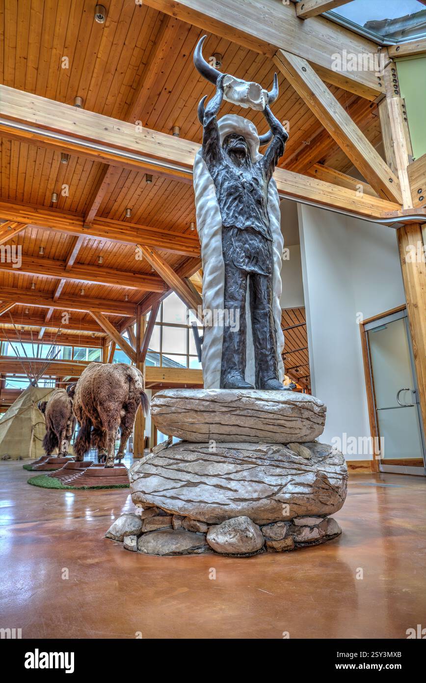 Statua di un uomo con la testa di bufalo. Ci sono due teste di bufalo sullo sfondo. La statua è su una roccia Foto Stock