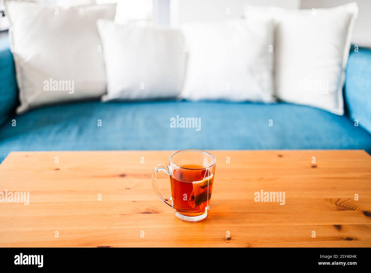 tazza di tè rooibos con teabag sul tavolino di fronte al divano blu con cuscini bianchi Foto Stock tazza di tè rooibos con teabag sul tavolino di fronte al divano blu con cuscini bianchi Foto Stock