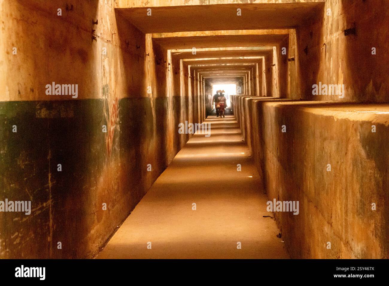 Sottopassaggio pedonale scarsamente illuminato con pareti in cemento consumato a Enugu, Nigeria, marzo 2025 una figura solitaria cammina verso l'uscita, incorniciata da simmetria geometrica Foto Stock