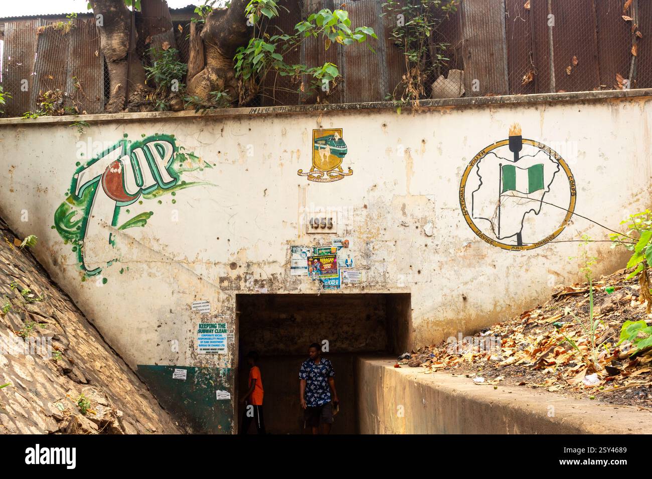 Sottopassaggio pedonale a Enugu, Nigeria, con murales sbiaditi e emblemi universitari, con alberi che crescono sopra, mostrando segni di degrado urbano, marzo 2025 Foto Stock
