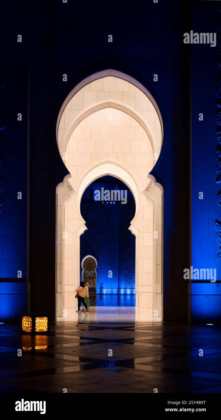 Arco islamico illuminato di notte con dettagli intricati e visitatori di passaggio, Una miscela di architettura mediorientale tradizionale e moderna Foto Stock