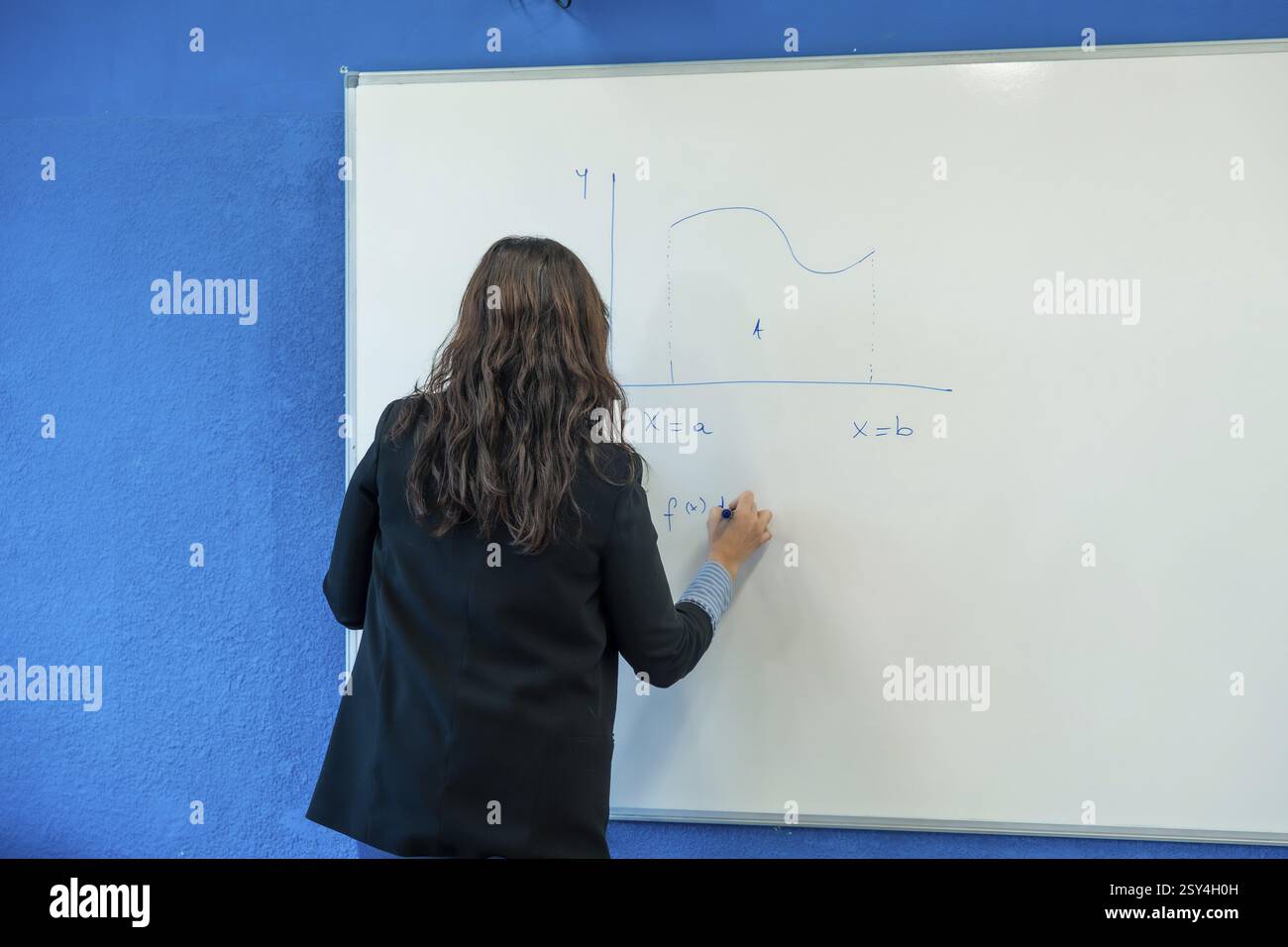 Professore universitario che spiega una funzione matematica agli studenti, scrivendo su una lavagna in classe Foto Stock