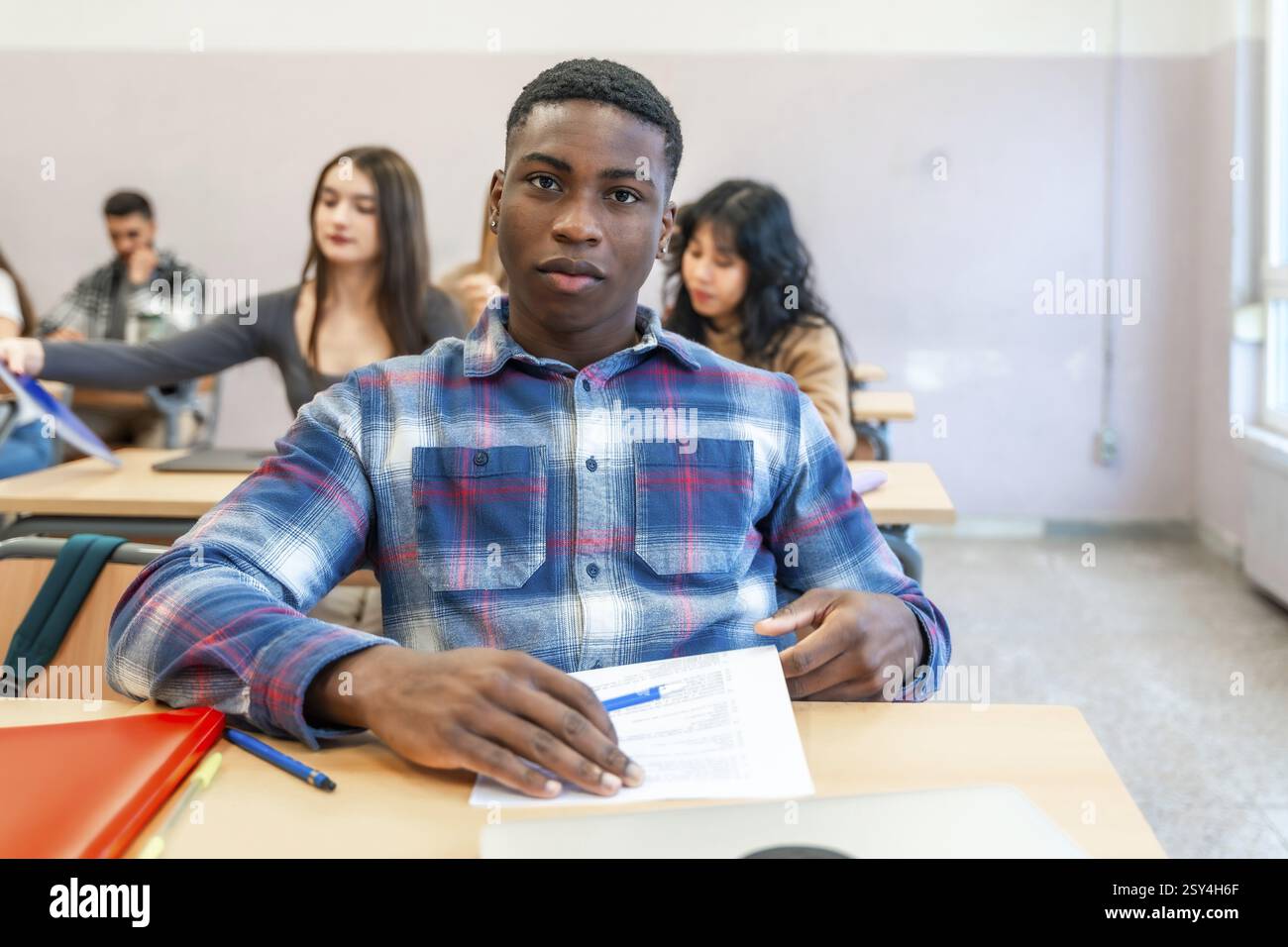 Giovane uomo di colore che si concentra sui suoi studi in una classe universitaria, circondato da compagni di studenti di diversa provenienza Foto Stock
