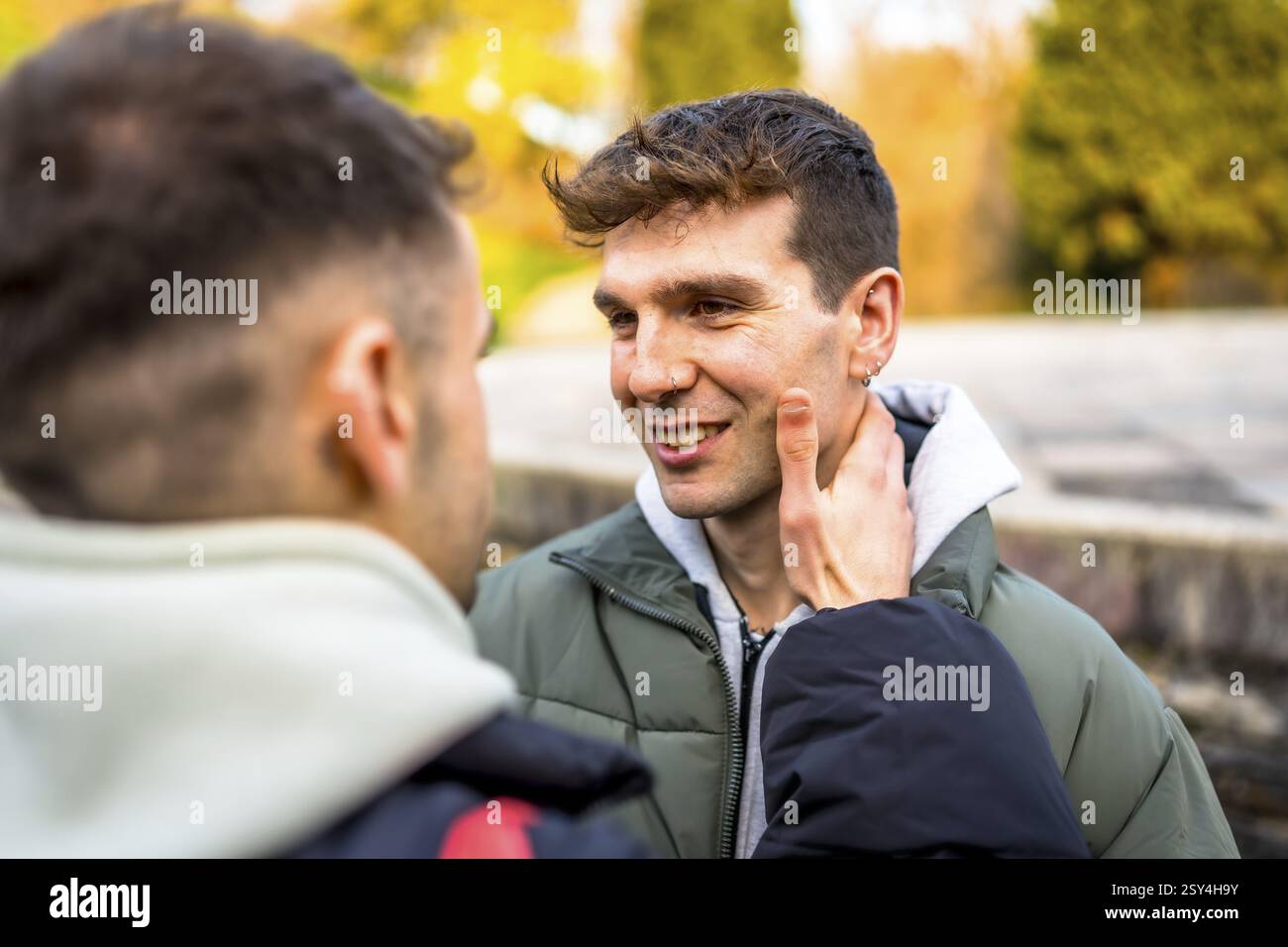 Due uomini che condividono un momento tenero in un parco, godendosi la compagnia dell'altro durante una splendida giornata autunnale Foto Stock