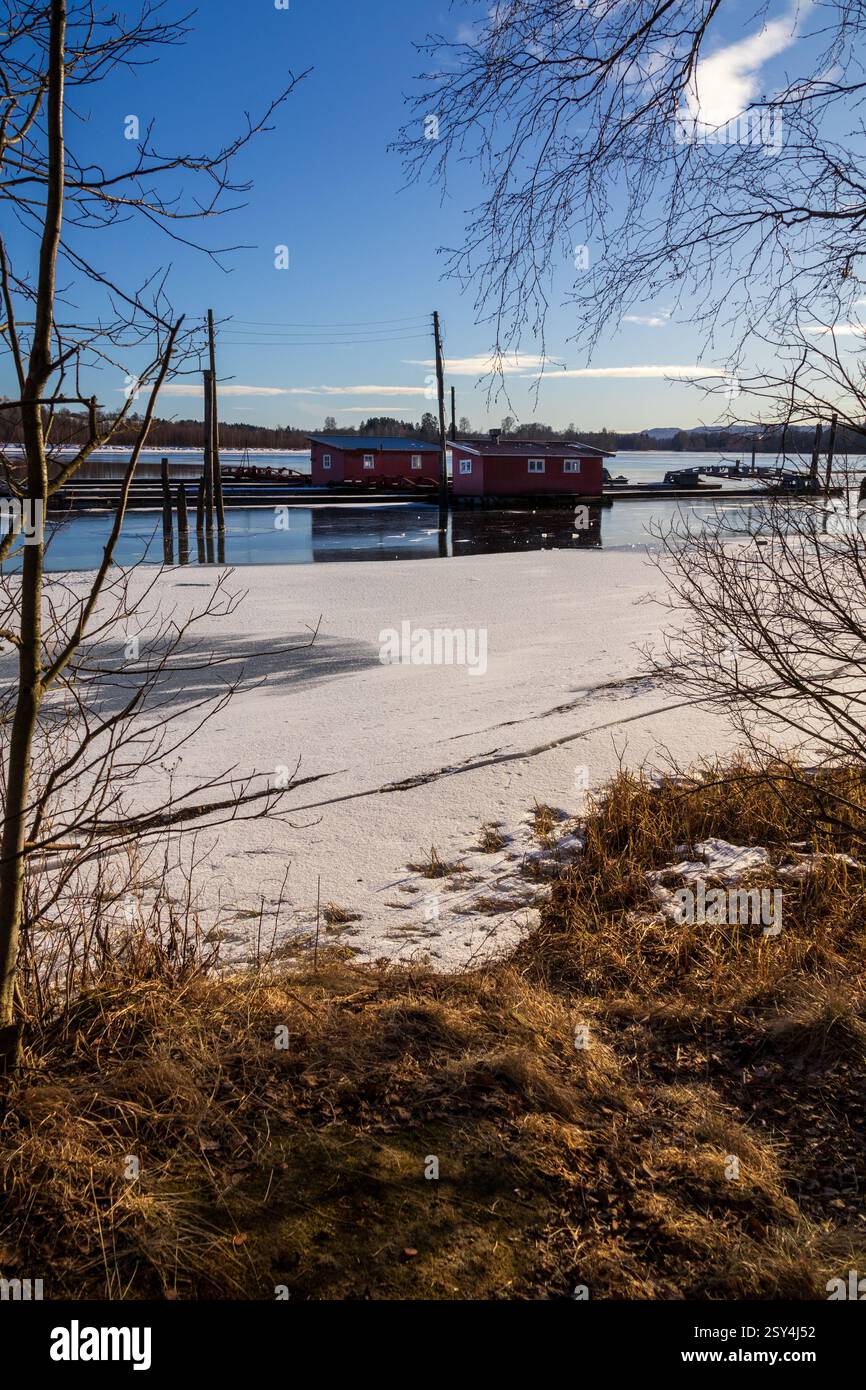 Sentieri ghiacciati: I pontoni riposano sul ghiaccio, portando a boatouses racchiuse nella morsa invernale, i loro riflessi scintillano sotto il luminoso sole invernale Foto Stock