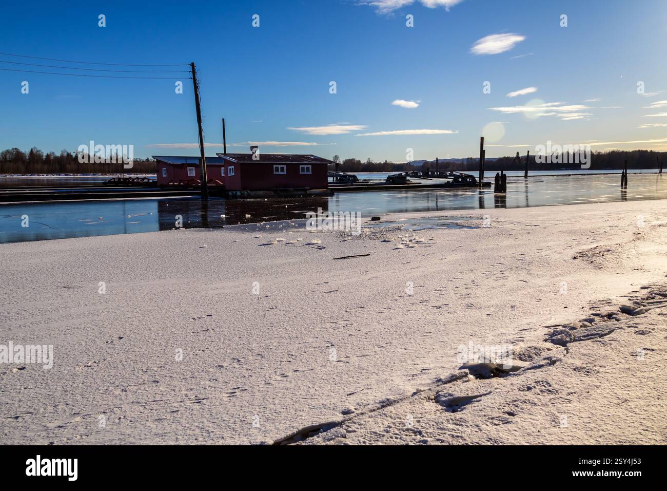 Sentieri ghiacciati: I pontoni riposano sul ghiaccio, portando a boatouses racchiuse nella morsa invernale, i loro riflessi scintillano sotto il luminoso sole invernale Foto Stock