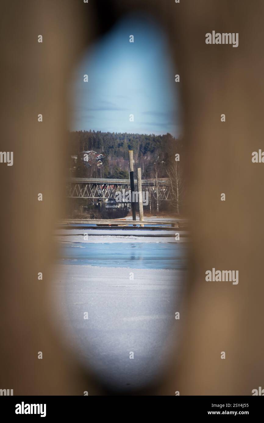 Uno sguardo alla storia, incastrando il passato attraverso l'occhio della natura. Un fiume ghiacciato, una vecchia struttura boschiva e un ponte visto attraverso la cavità di un albero Foto Stock
