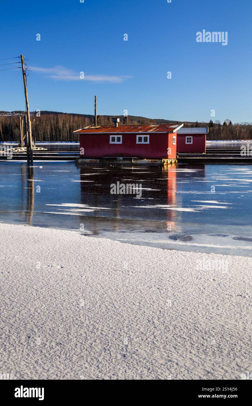 Sentieri ghiacciati: I pontoni riposano sul ghiaccio, portando a boatouses racchiuse nella morsa invernale, i loro riflessi scintillano sotto il luminoso sole invernale Foto Stock