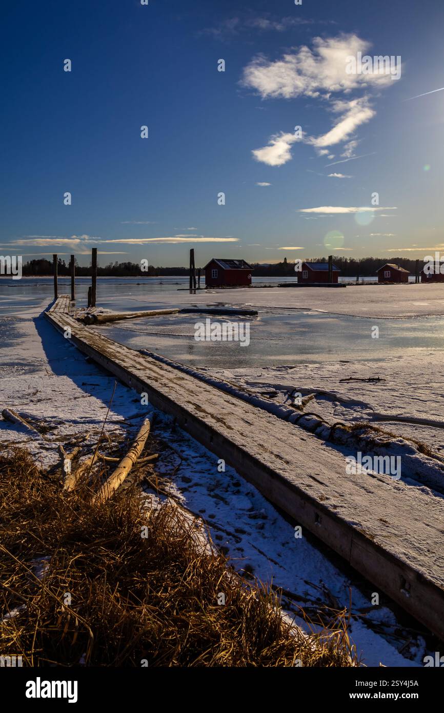 Sentieri ghiacciati: I pontoni riposano sul ghiaccio, portando a boatouses racchiuse nella morsa invernale, i loro riflessi scintillano sotto il luminoso sole invernale Foto Stock
