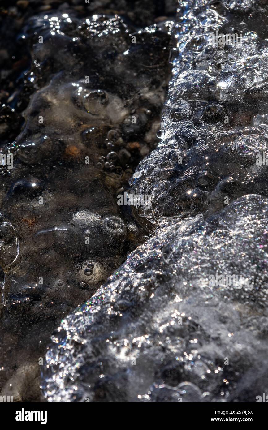 Dove il ghiaccio incontra l'acqua, le formazioni cristalline e le correnti fluenti si fondono in un delicato equilibrio, rivelando l'arte astratta della natura in perfetta chiarezza Foto Stock