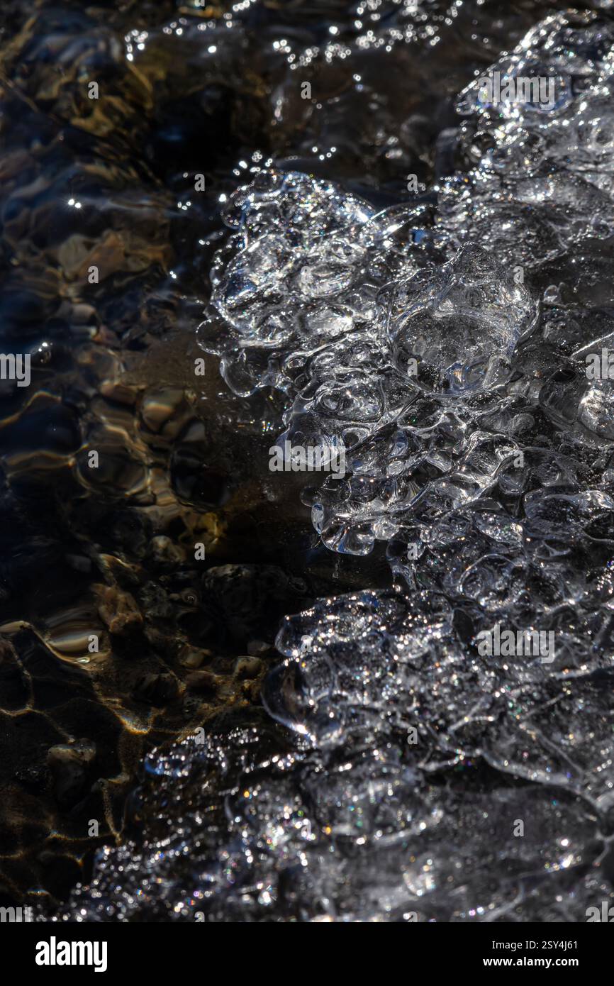 Dove il ghiaccio incontra l'acqua, le formazioni cristalline e le correnti fluenti si fondono in un delicato equilibrio, rivelando l'arte astratta della natura in perfetta chiarezza Foto Stock
