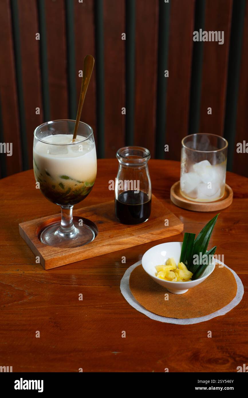 Es Cendol, una bevanda tradizionale indonesiana a base di latte di cocco, aggiunta con sciroppo di zucchero di palma e gelatina di farina di riso verde aromatizzata al panda, servita in compagnia Foto Stock