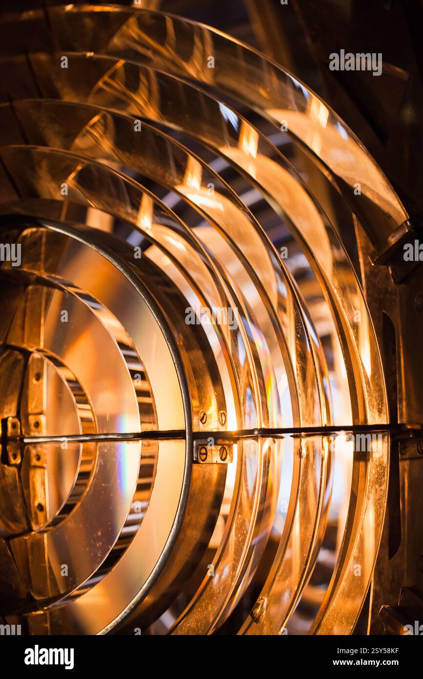 Lente Fresnel illuminata che mostra la sua complessa struttura in vetro e la calda luce soffusa. L'immagine cattura la precisione ottica e la maestria artistica Foto Stock