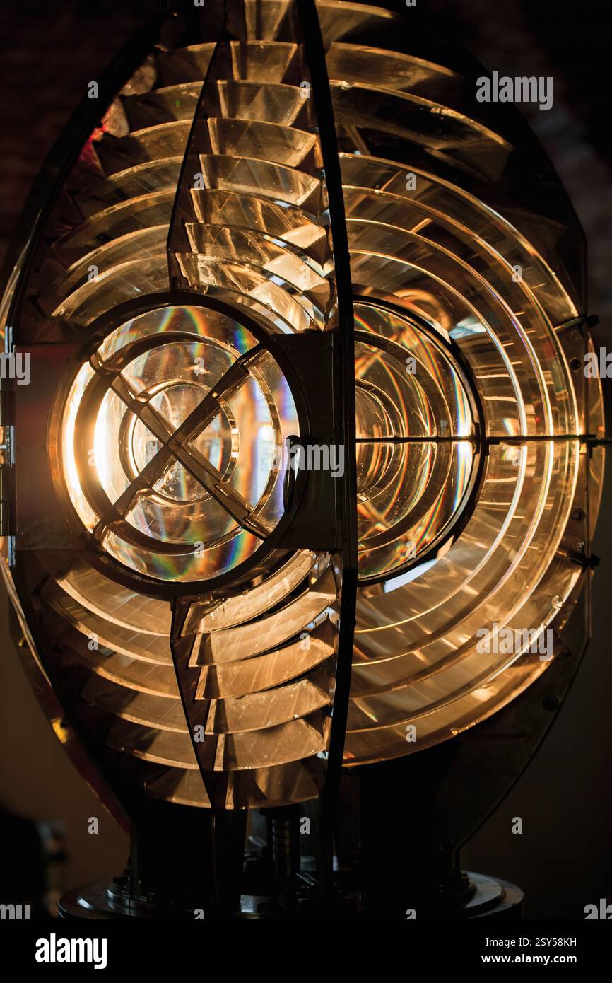 Una vista dettagliata di una lente Fresnel illuminata, che mostra la sua complessa struttura in vetro e la calda luce soffusa. L'immagine acquisisce la precisione ottica e una Foto Stock