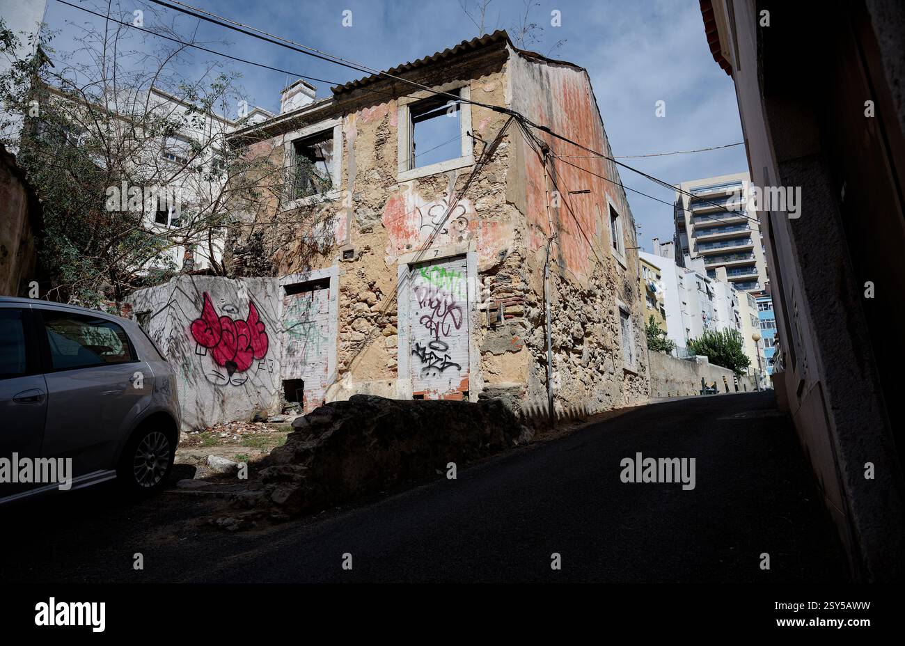 Edificio abbandonato con mura e graffiti sbriciolati in una stretta strada in salita a Lisbona Foto Stock