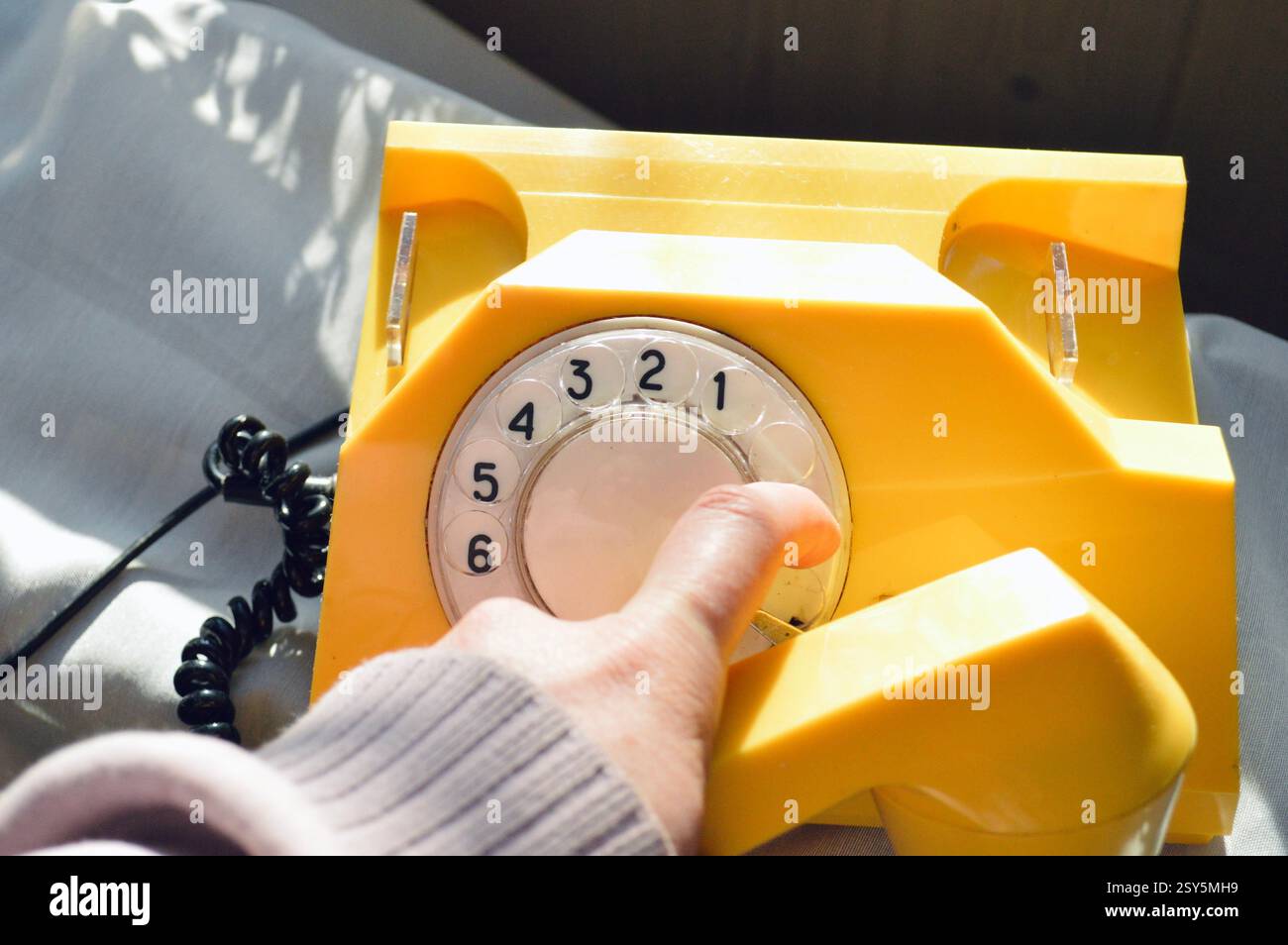 Una persona compone un numero su un vivace telefono rotativo giallo vintage dal design classico. Foto Stock