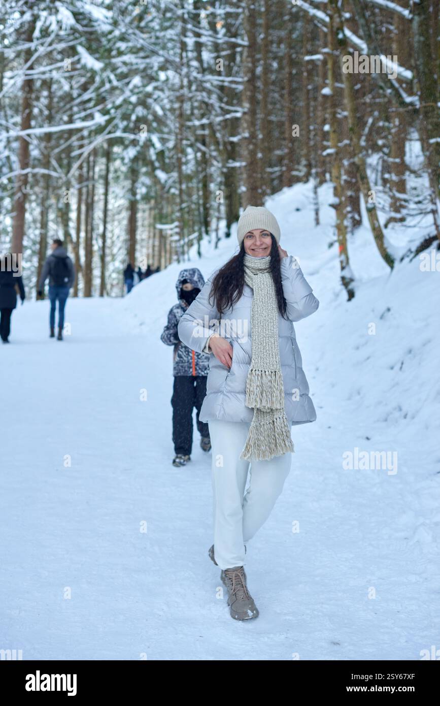Una fotografia ad alta risoluzione che cattura una tranquilla scena invernale in una foresta innevata. Una donna con lunghi capelli scuri cammina con sicurezza lungo un pa innevato Foto Stock