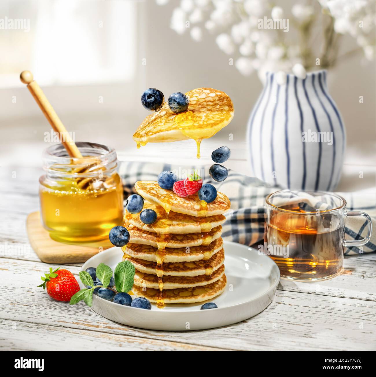 Deliziosi pancake sono conditi con miele dorato e adornati magnificamente con mirtilli e fragole freschi per una colazione romantica Foto Stock