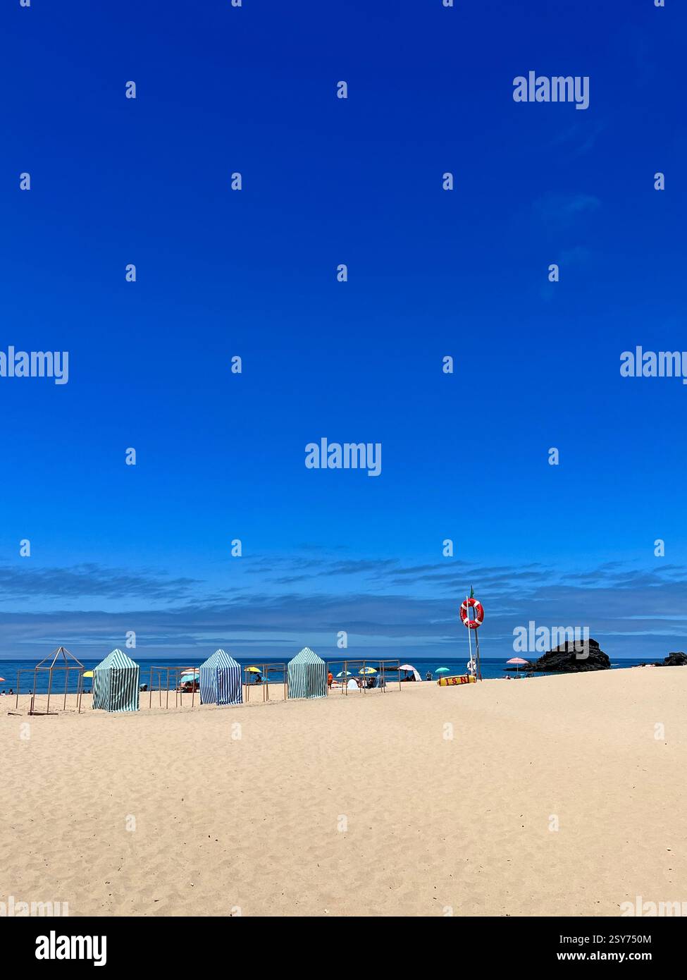 Una spiaggia tranquilla con tende a strisce, ombrelloni e un salvagente sotto un cielo azzurro. Foto Stock