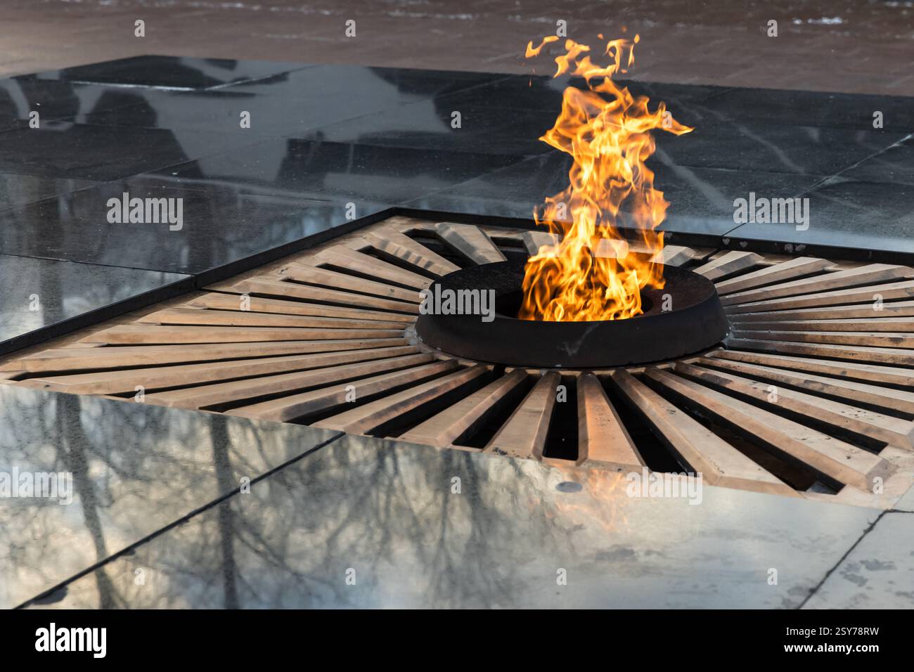 Una fiamma eterna simbolica che brucia in una struttura circolare con superfici riflettenti e fuoco vibrante, che rappresenta la memoria e l'onore in un ambiente sereno e sereno Foto Stock