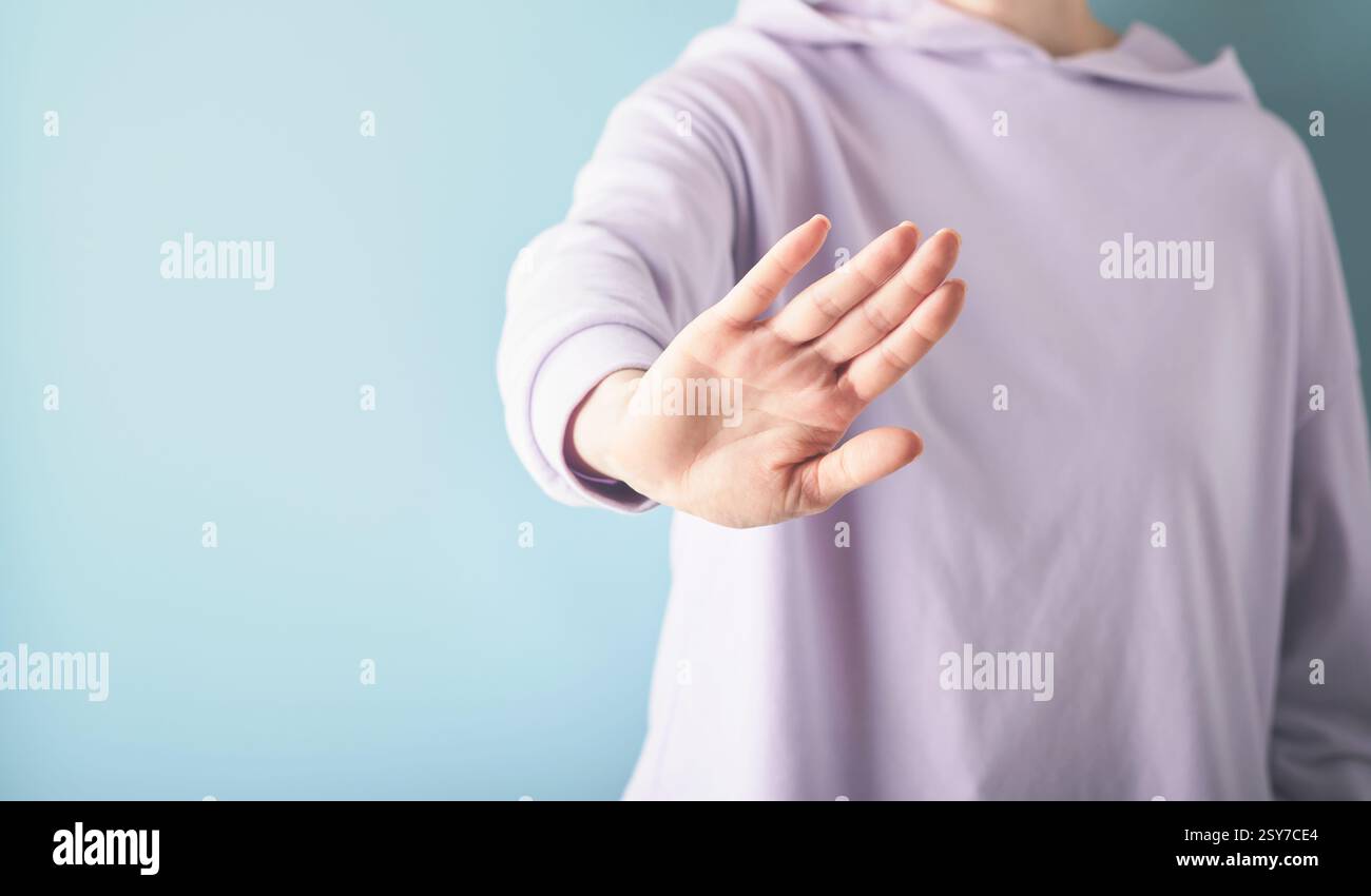 Vista corta di una giovane donna adulta che indossa o indossa un'elegante felpa lilla, che fa stop con un palmo su sfondo blu e spazio per le copie Foto Stock